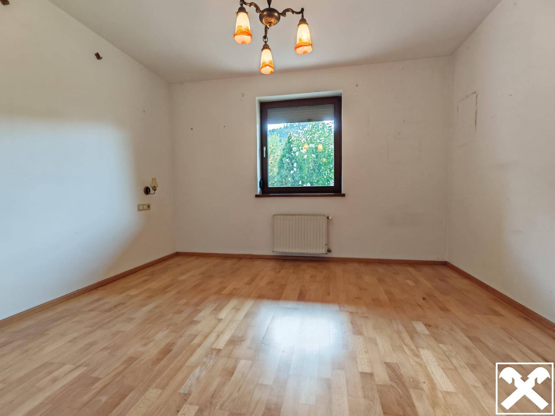 Leeres Schlafzimmer mit Parkettboden, einem Fenster und einem Heizkörper.