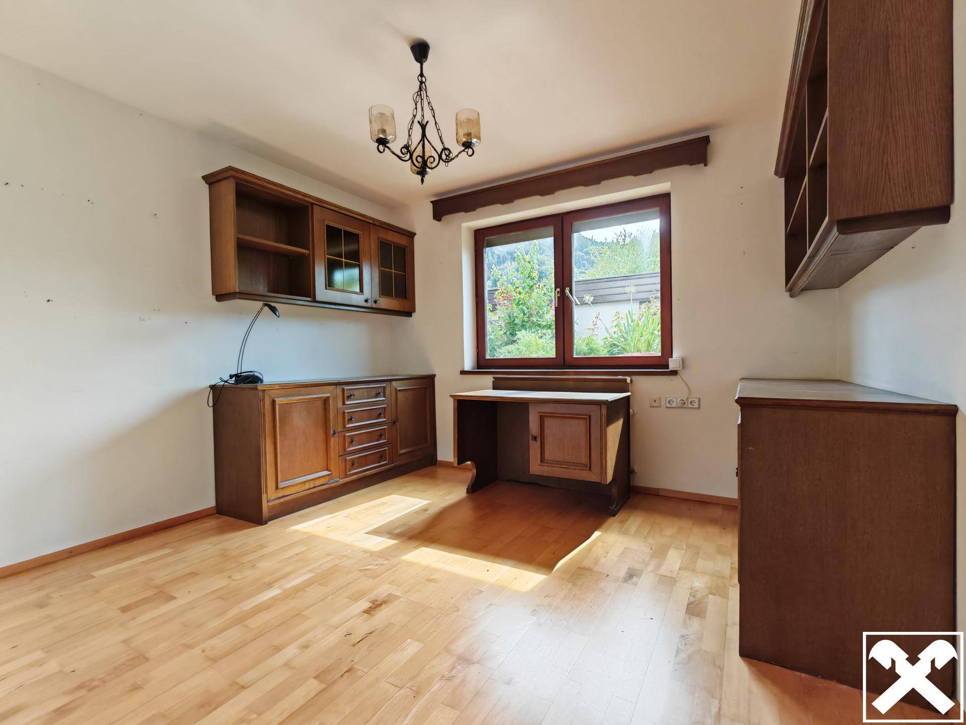 Arbeitszimmer mit Holzmöbeln, Parkettboden und Blick ins Grüne durch das Fenster.