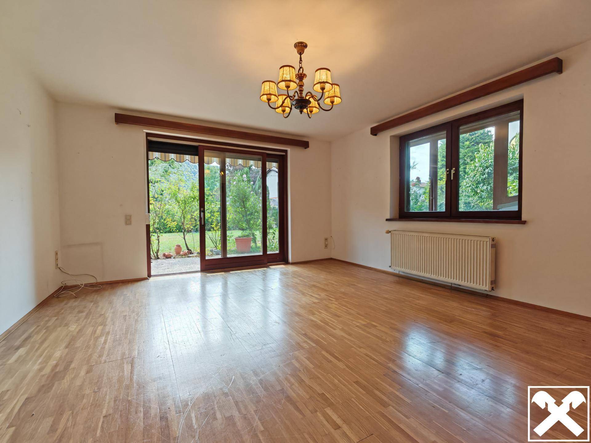 Helles Wohnzimmer mit Parkettboden und Zugang zum Garten durch eine große Schiebetür.