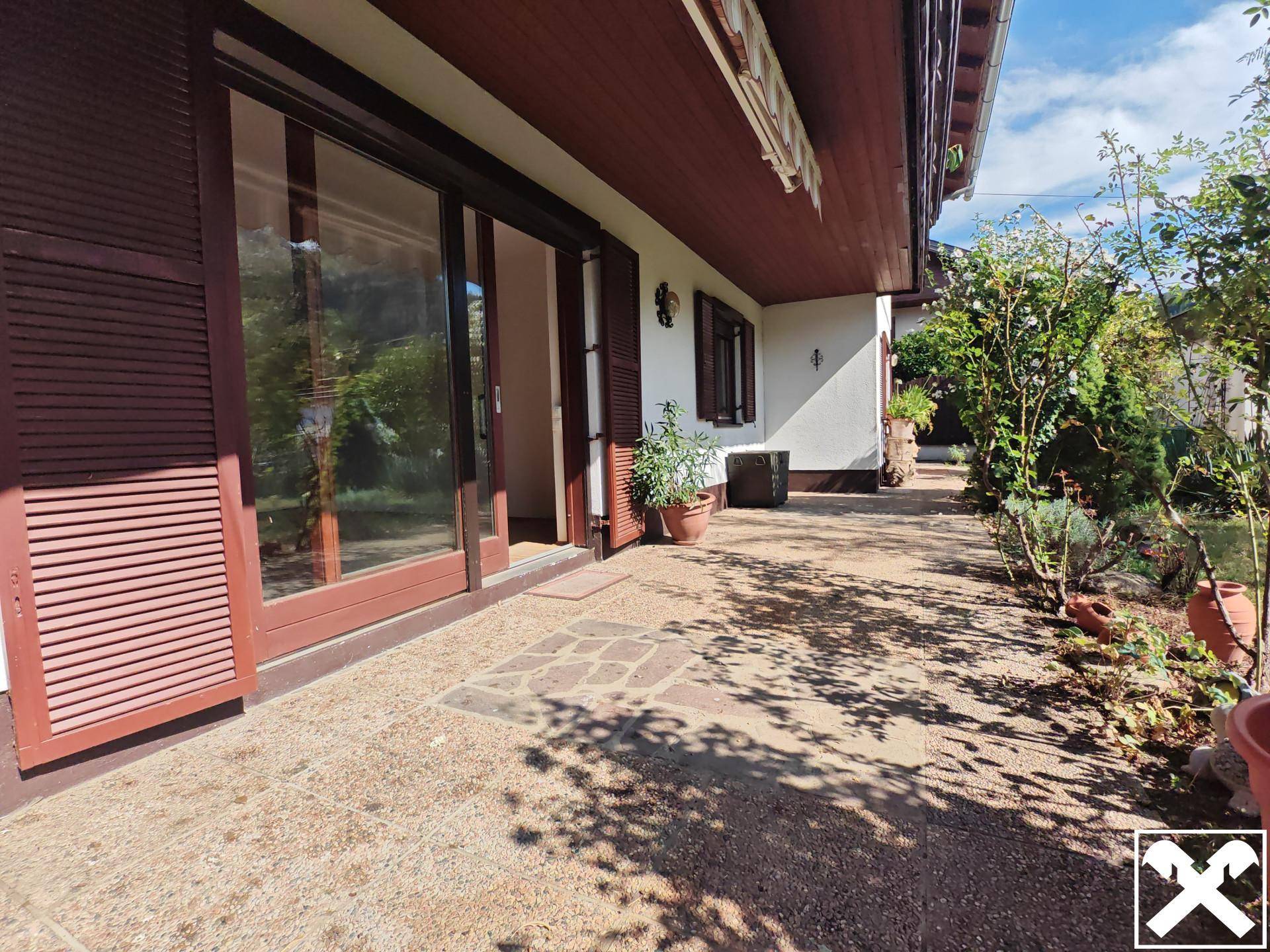 Gepflasterte Terrasse entlang des Hauses mit Zugang zu Innenräumen und Pflanzen.