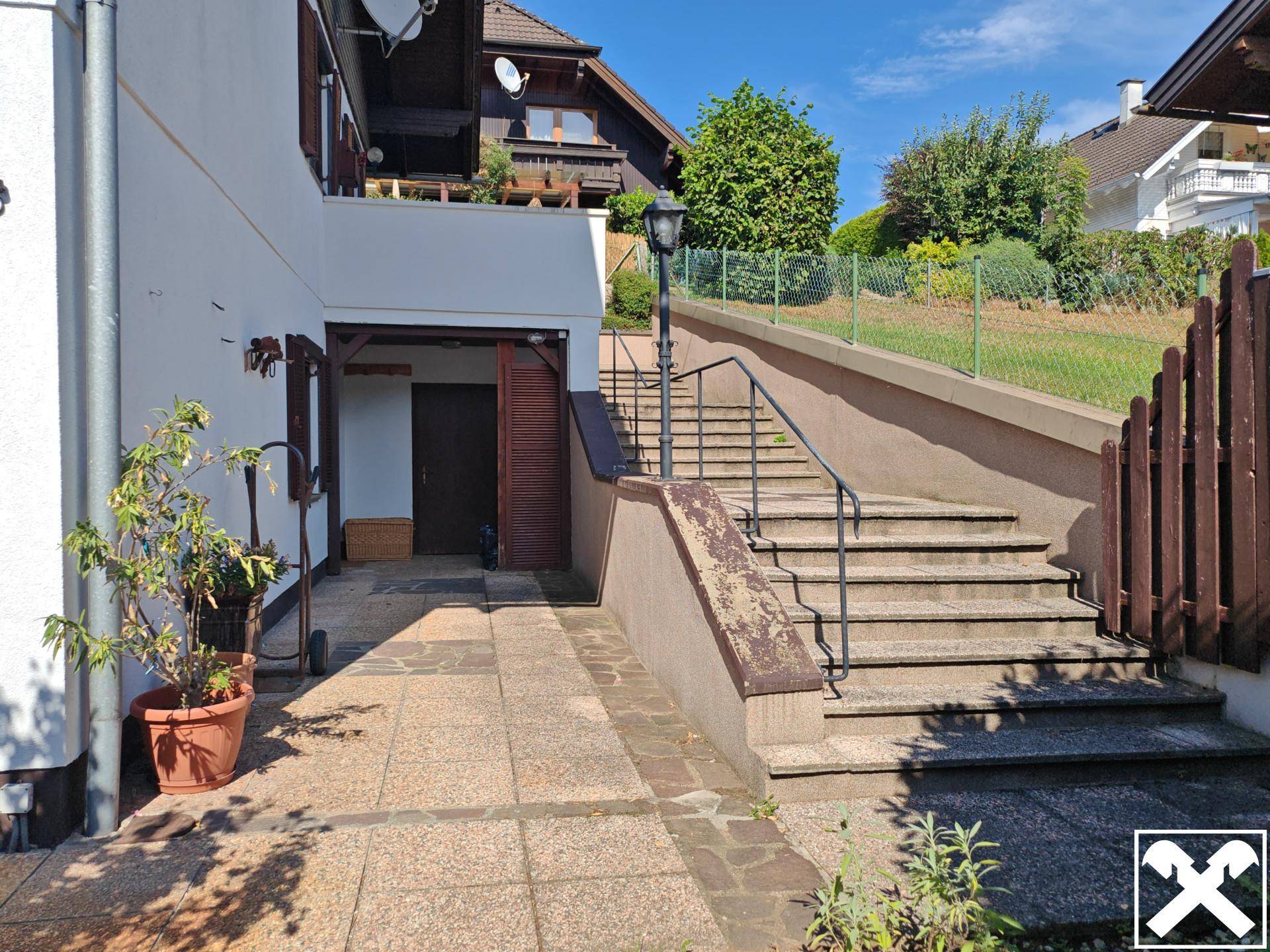 Außentreppe führt zum Untergeschoss des Hauses, umgeben von Grünflächen.
