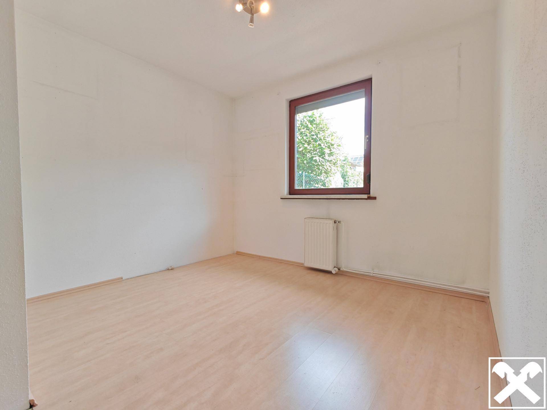 Helles Schlafzimmer mit Laminatboden, einem Fenster und einem Heizkörper.