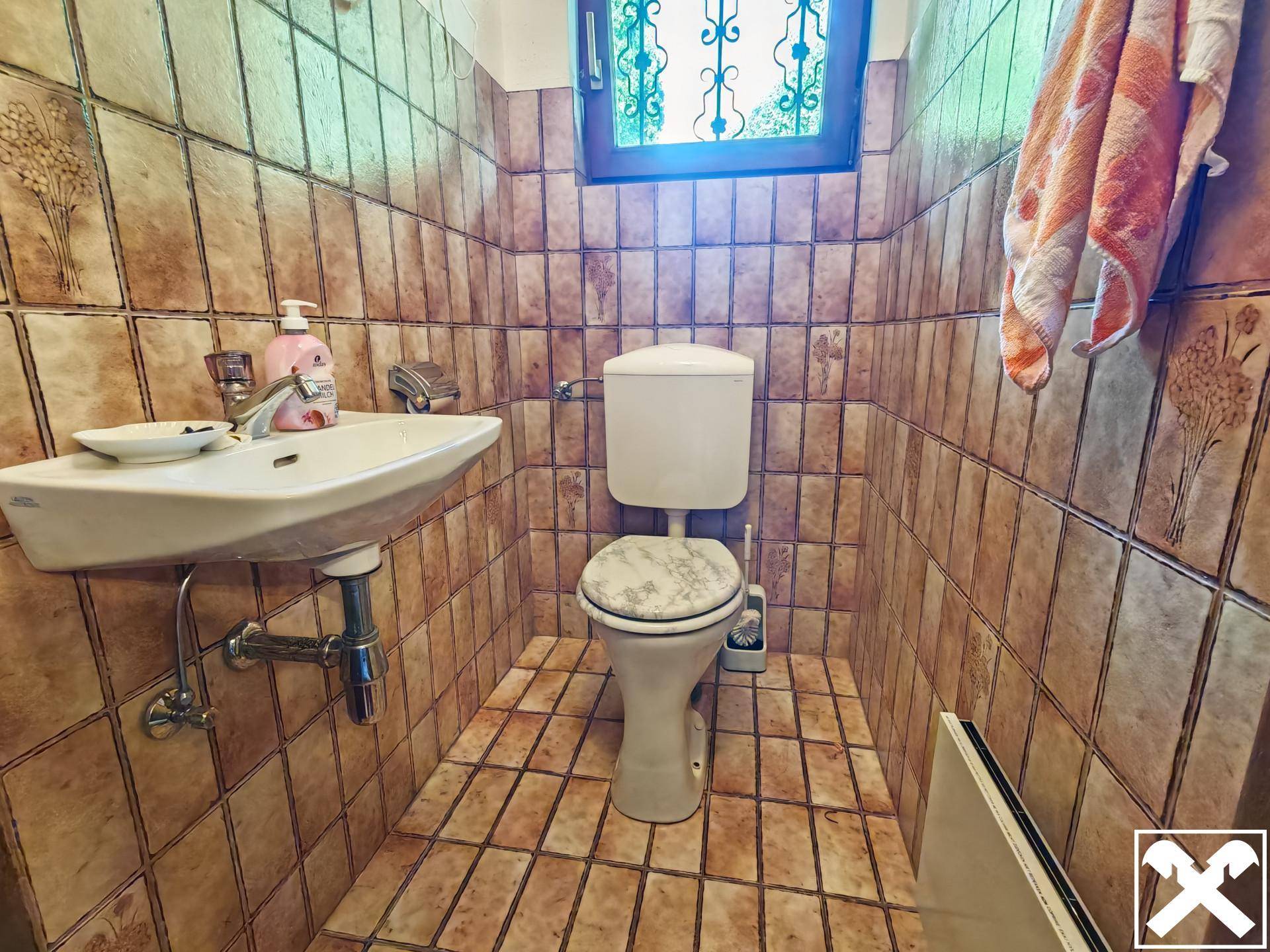Kleines Gäste-WC mit Waschbecken und WC, komplett gefliest in warmen Brauntönen.