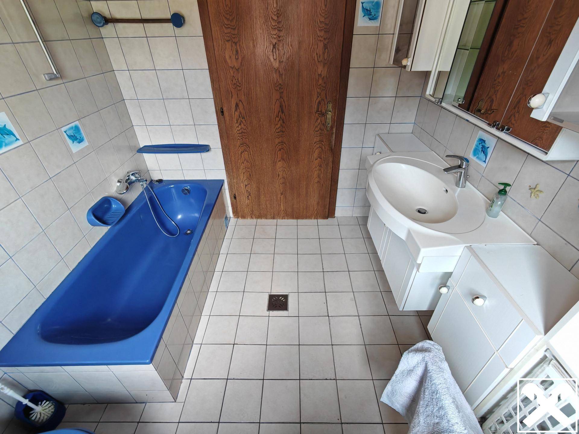 Badezimmer mit blauer Badewanne, Waschbecken und WC, gefliest in hellen Farben.