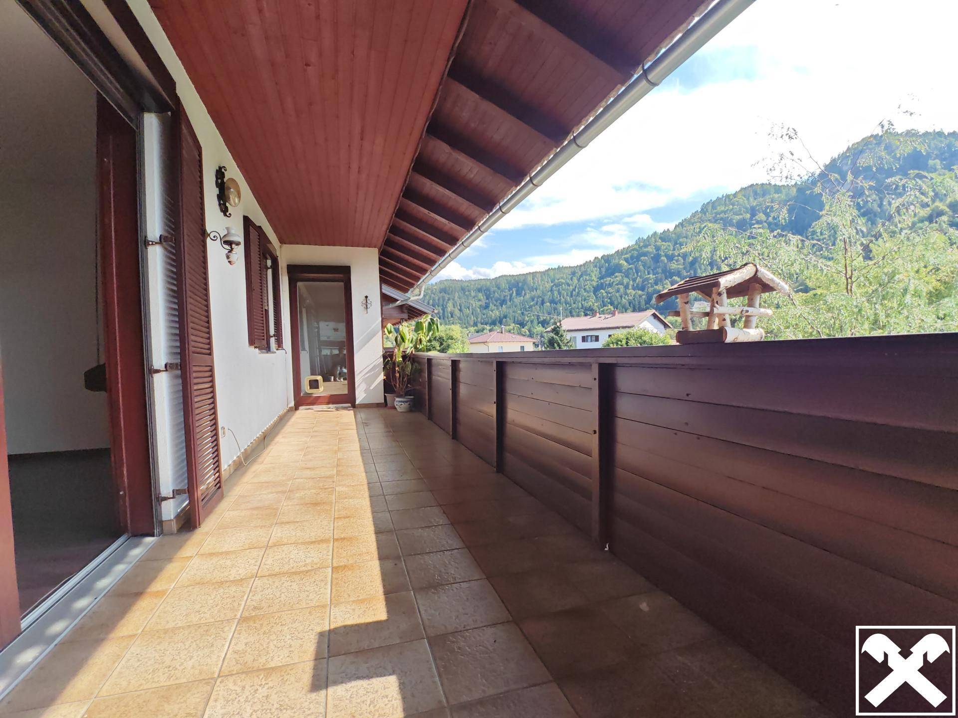 Langer Balkon mit Fliesenboden, Holzverkleidung und weitem Bergblick unter blauem Himmel.