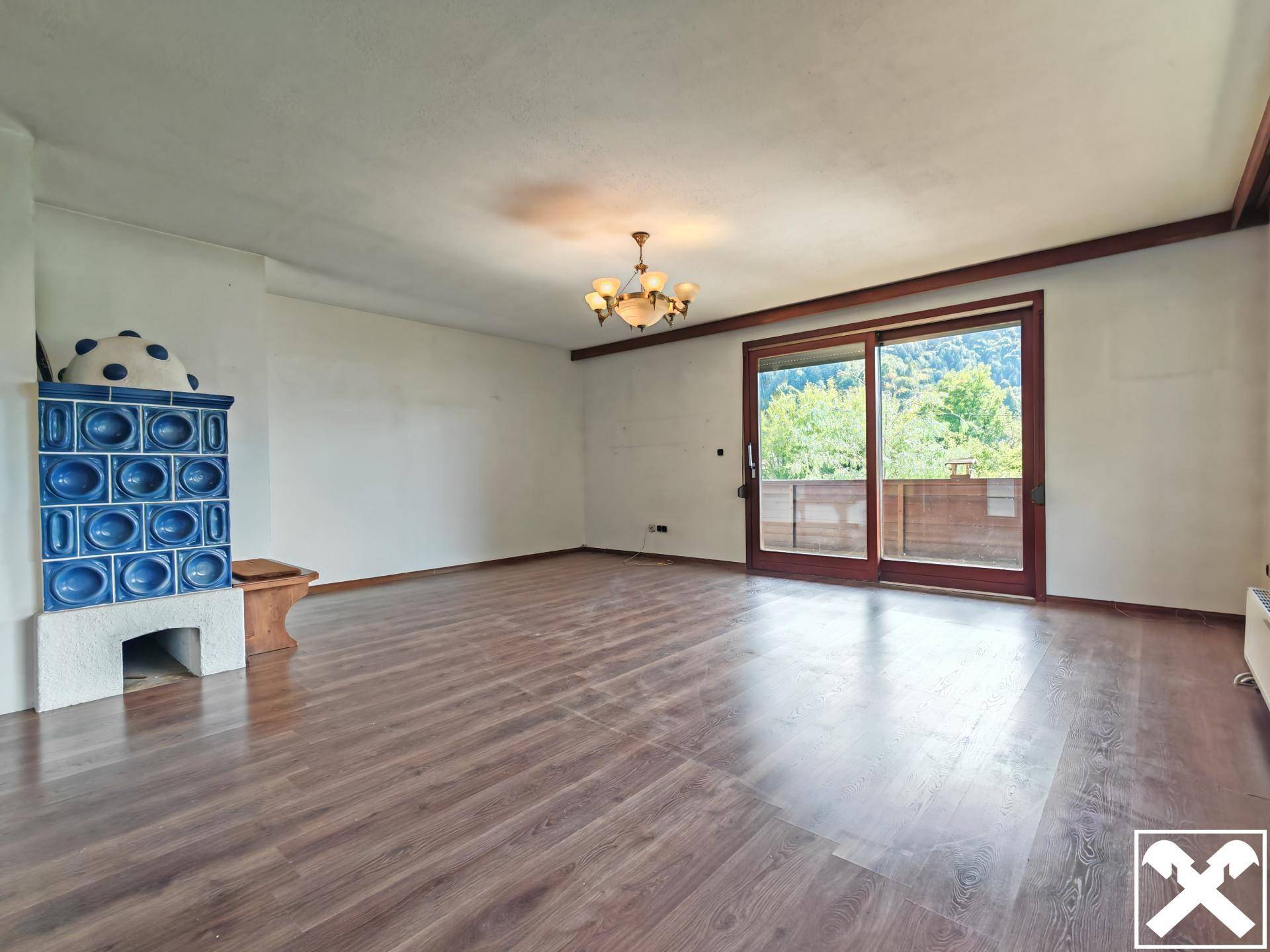 Helles Wohnzimmer mit Laminatboden, Kachelofen und Zugang zu einem Balkon.