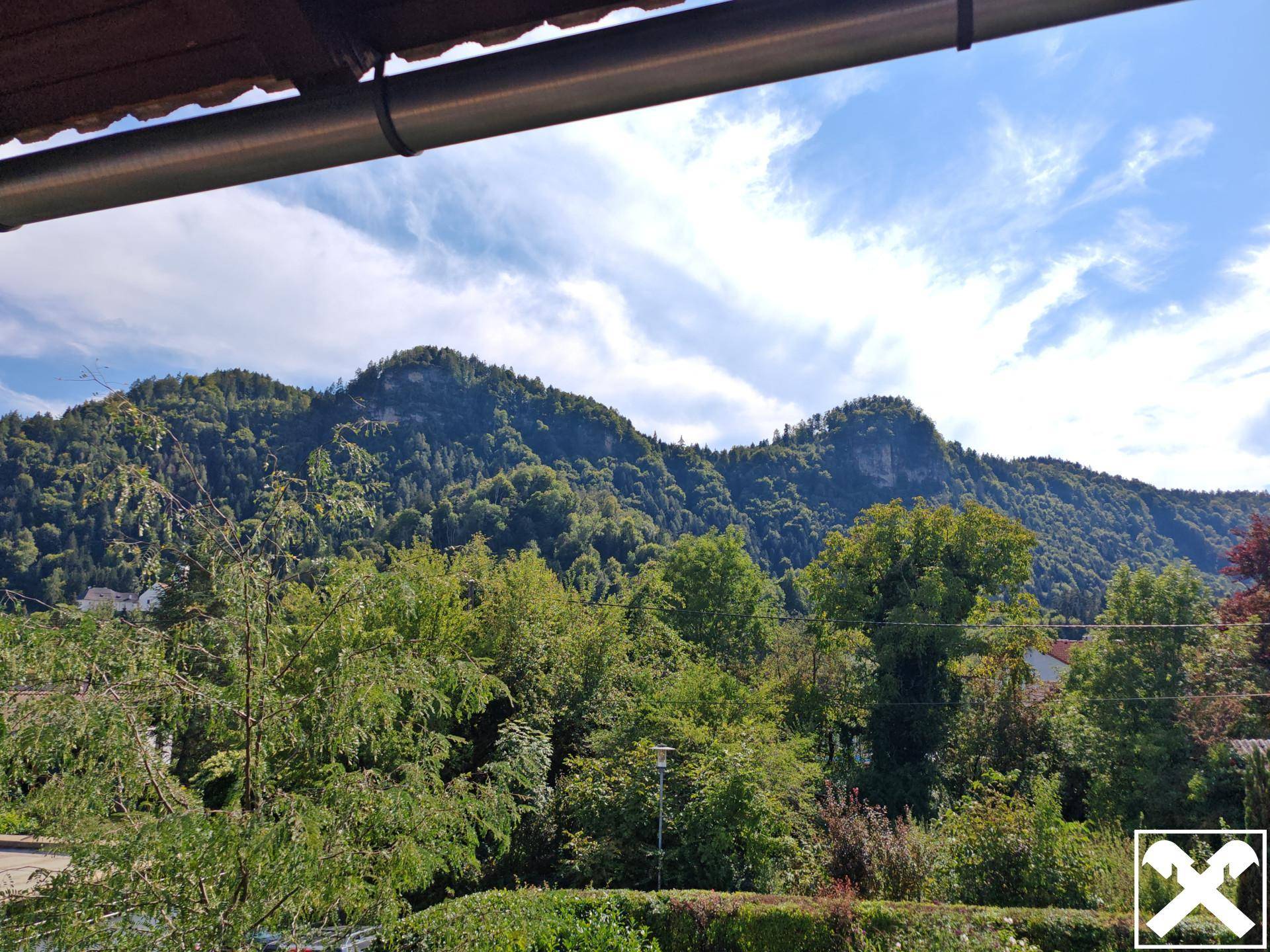 Panoramablick auf bewaldete Berge und grüne Landschaft unter einem strahlend blauen Himmel.