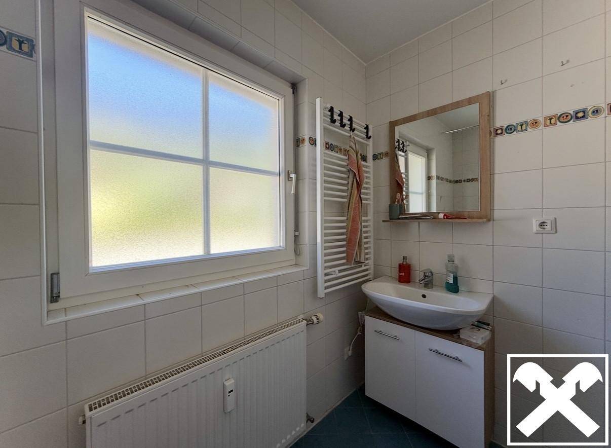 Badezimmer mit hellen Fliesen, Fenster, modernem Waschbeckenunterschrank und Handtuchheizkörper.