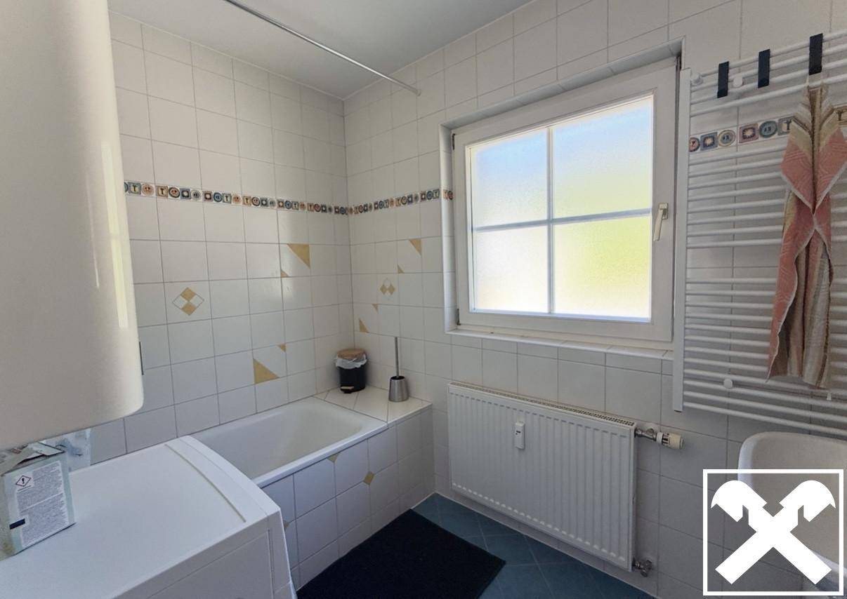 Gefliestes Badezimmer mit Badewanne, Fenster und Heizkörper für Handtücher.