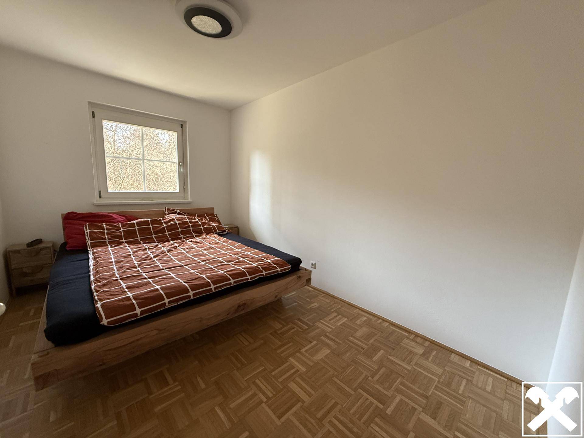 Helles Schlafzimmer mit Parkettboden und einem großen Fenster für viel Tageslicht.