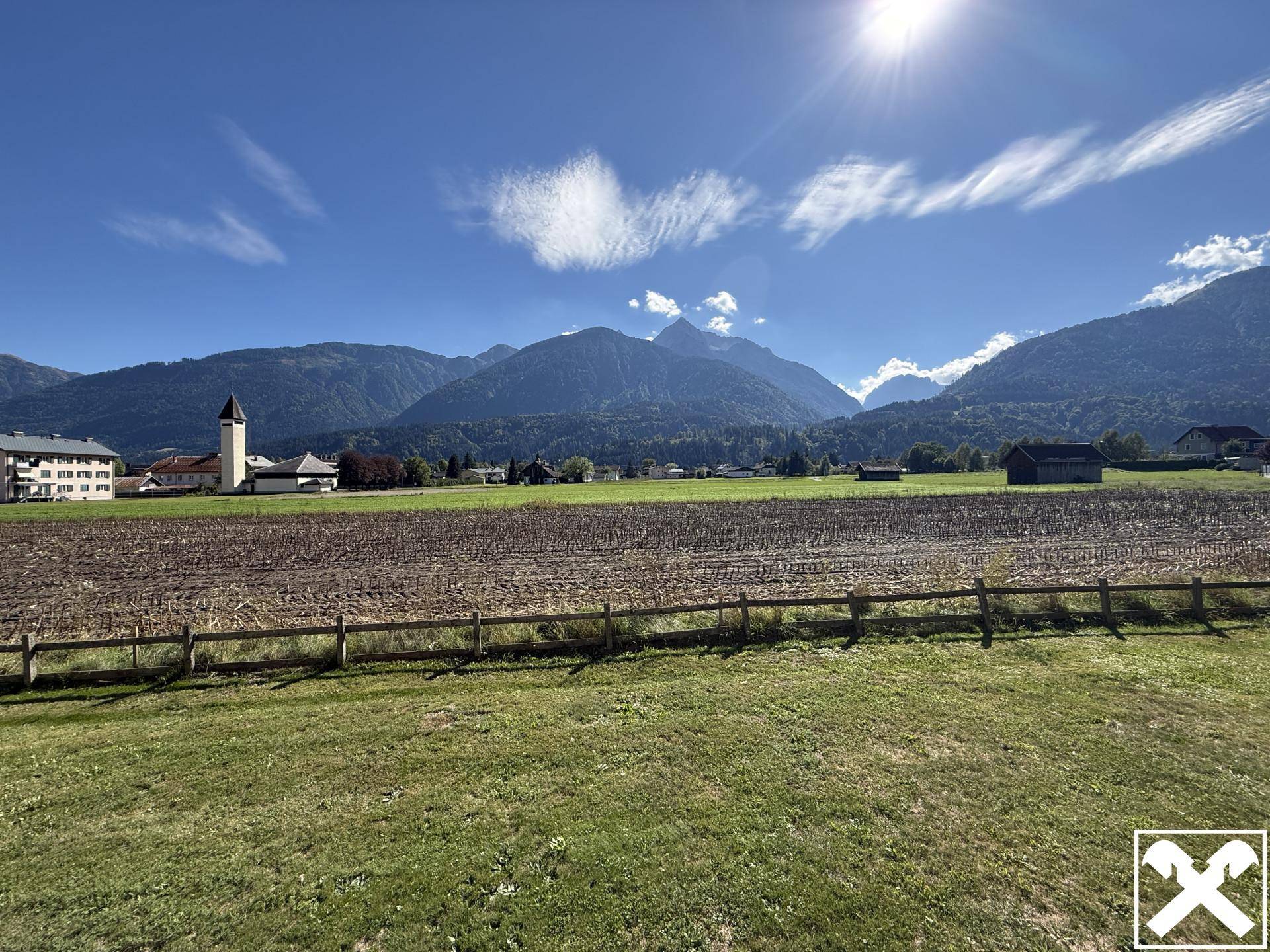 Weitläufiger Blick über Felder und Berge unter blauem Himmel mit Sonnenschein.