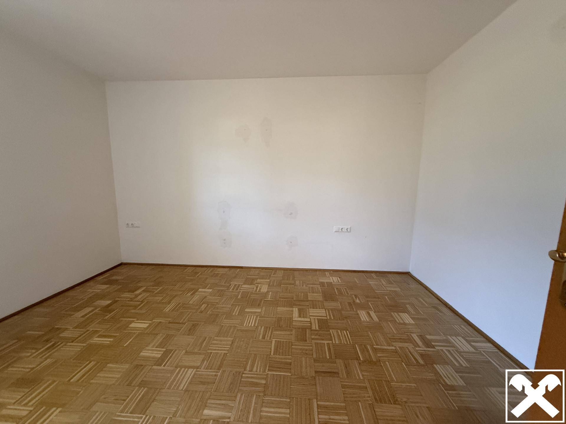 Helles Zimmer mit Parkettboden und weißen Wänden, ideal für ein Schlaf- oder Wohnzimmer.