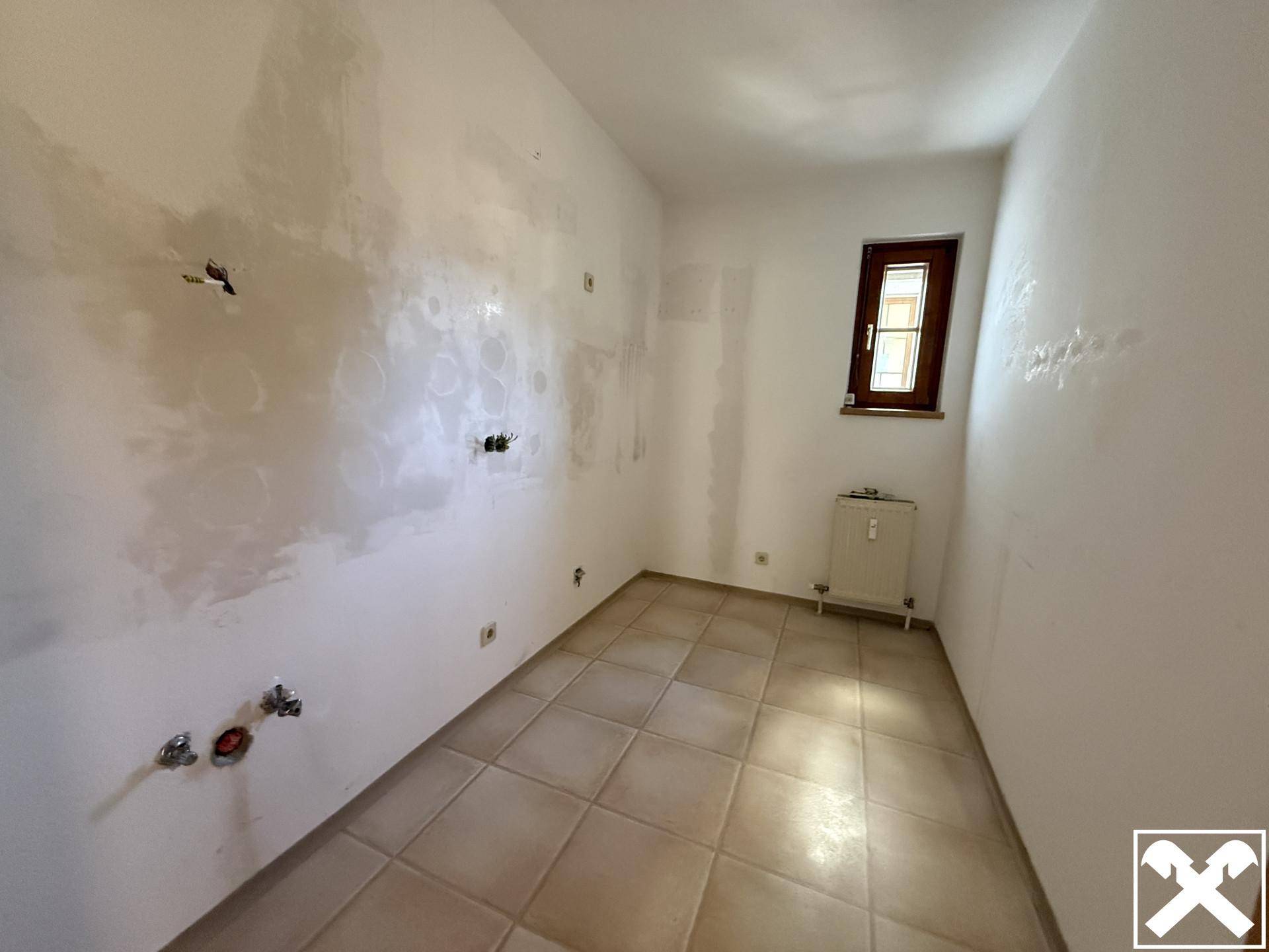 Unmöblierte Küche mit Fliesenboden und Fenster, vorbereitet für die Installation einer Einbauküche.