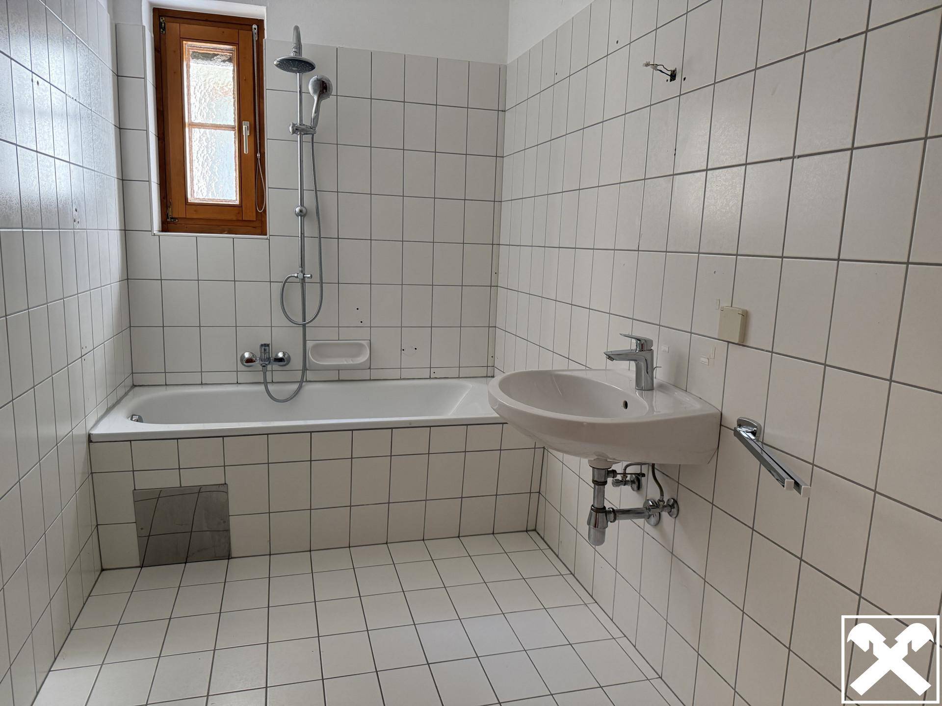 Badezimmer mit Badewanne, Waschbecken und weißen Fliesen, ausgestattet mit einem Fenster.