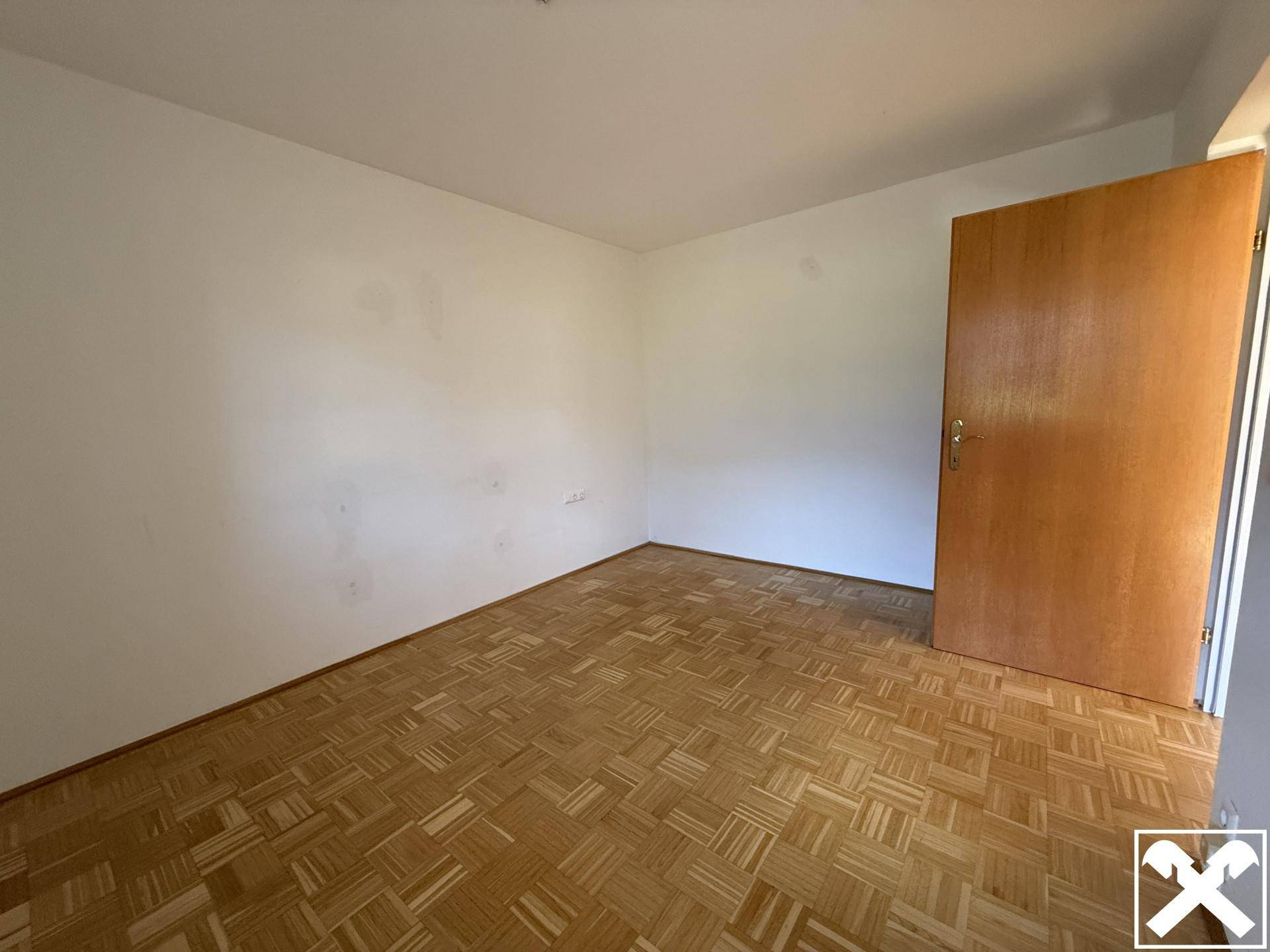 Leeres Zimmer mit Parkettboden und Holztür, bietet vielseitige Nutzungsmöglichkeiten.