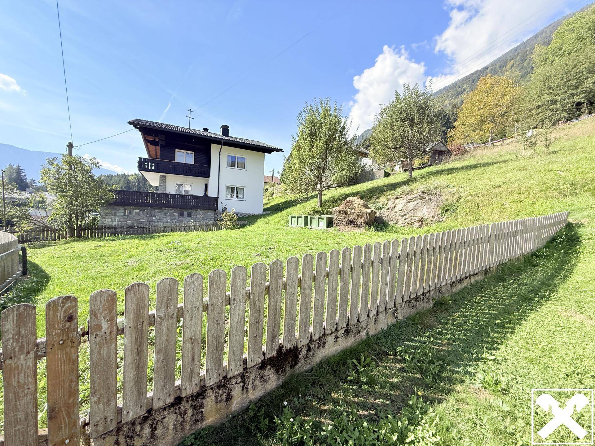 Haus in Hanglage mit großem Gartenbereich und Holzzaun, umgeben von Natur.