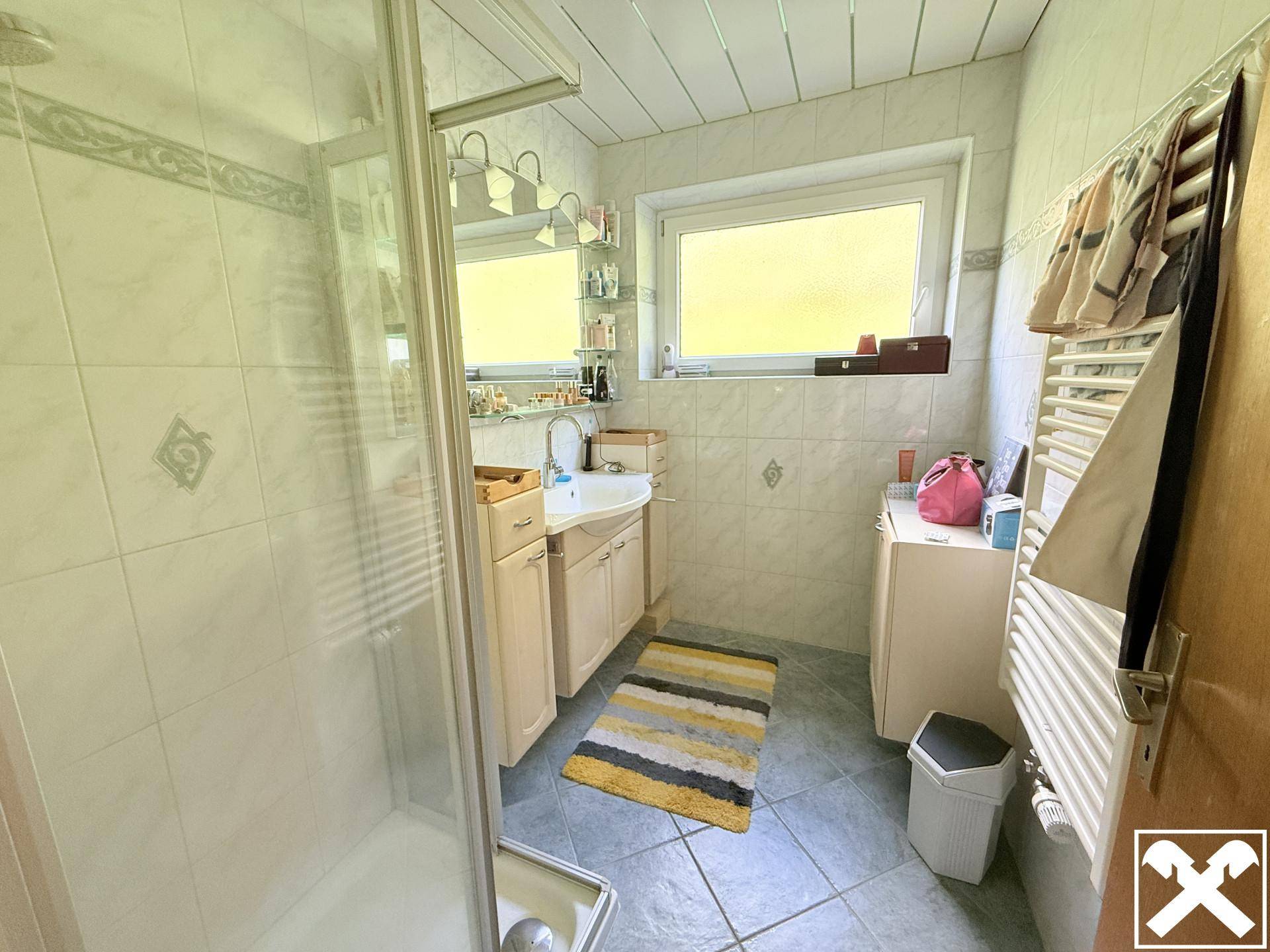 Helles Badezimmer mit Dusche, Fenster und Waschtischunterschrank.