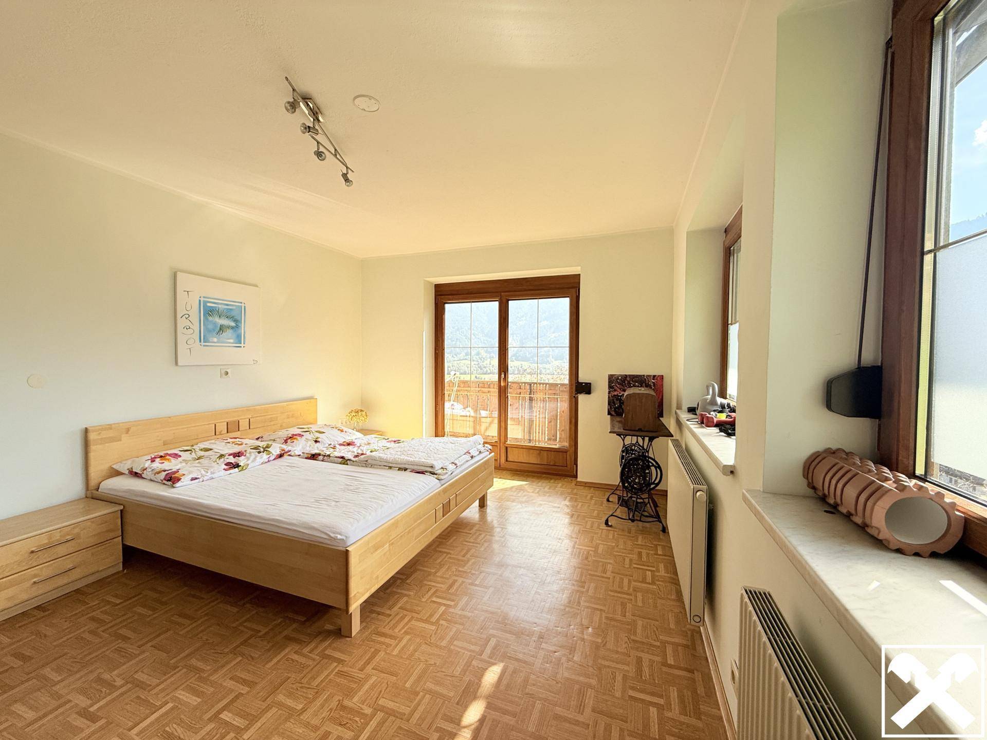 Helles Schlafzimmer mit Holzbett, Parkettboden und Balkonzugang mit Bergblick.