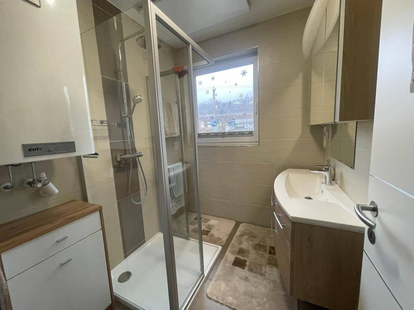Helles Badezimmer mit Dusche, Waschbecken und Fenster.