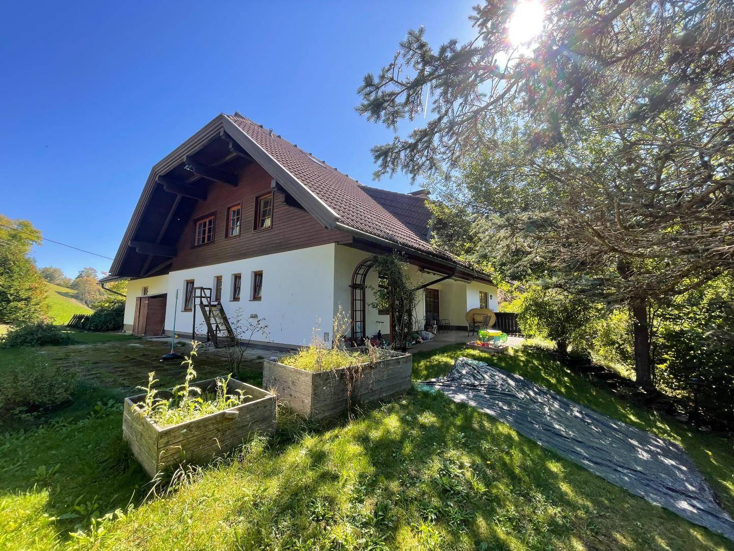 Sonnige Gartenseite des Hauses mit erhöhten Beeten und viel Grün in ländlicher Umgebung.