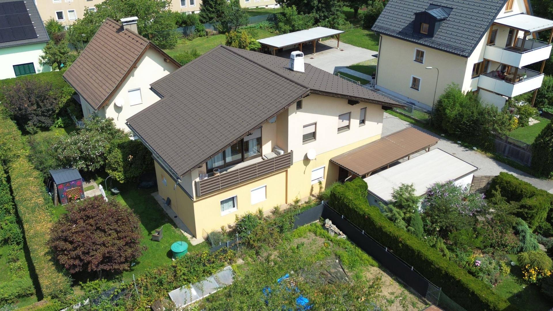 Luftaufnahme eines Wohnhauses mit Balkon, braunem Dach und umgebenden Gärten in einer ruhigen Wohngegend.