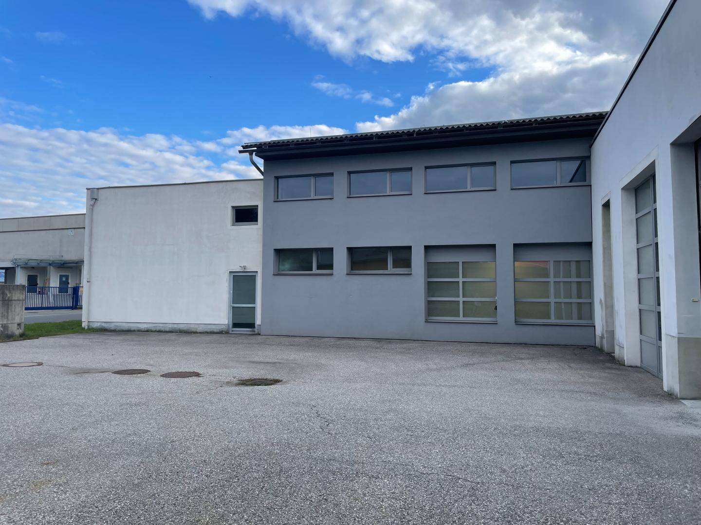 Rückansicht eines Gewerbegebäudes mit grauer Fassade, mehreren Fenstern und einem Nebeneingang unter blauem Himmel.