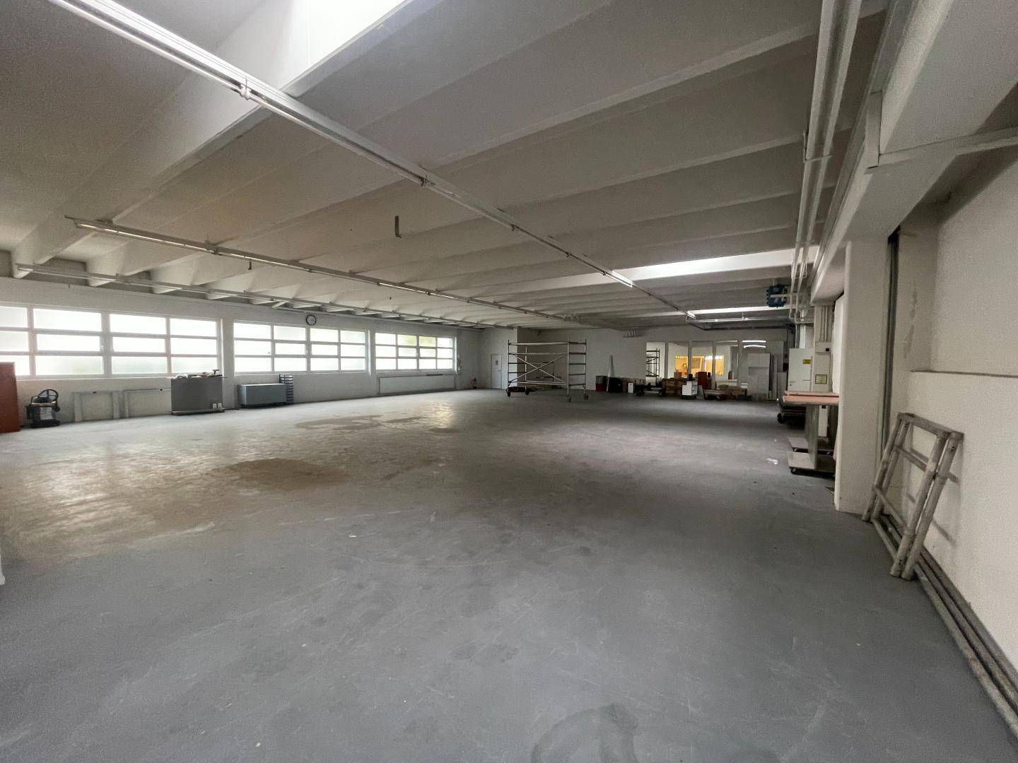 Geräumige, leere Lagerhalle mit vielen Fenstern, hohen Decken und einem robusten Betonboden, bereit zur Nutzung.