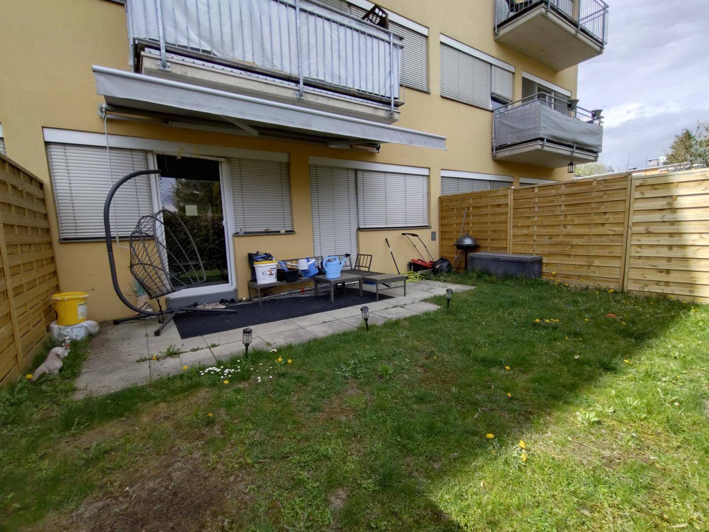 Kleiner Gartenbereich mit Terrasse, Rasenfläche und Holzzaun für Privatsphäre.
