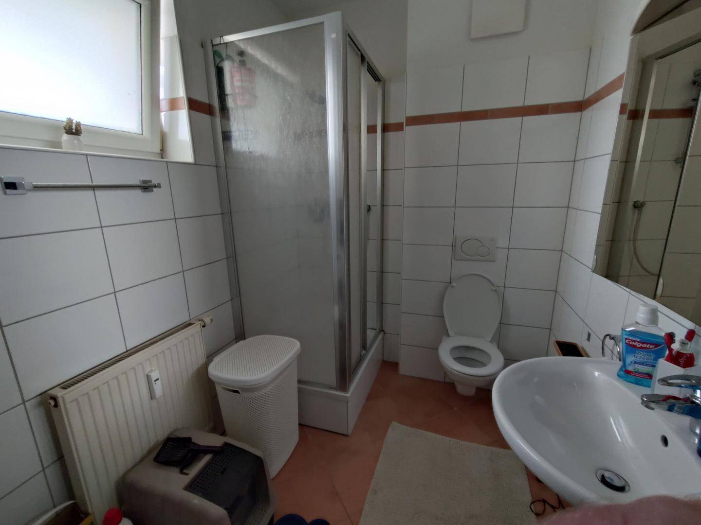 Badezimmer mit Duschkabine, WC, Waschbecken und Fenster, gefliest in hellen Tönen.