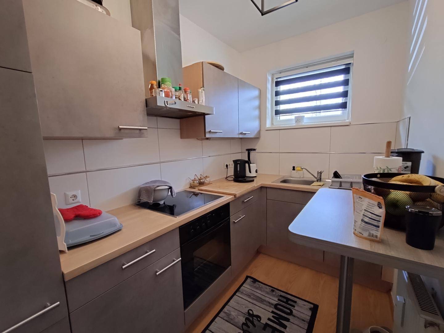 Kleine, moderne Küche mit grauen Schränken, Holzarbeitsplatte und Fenster.