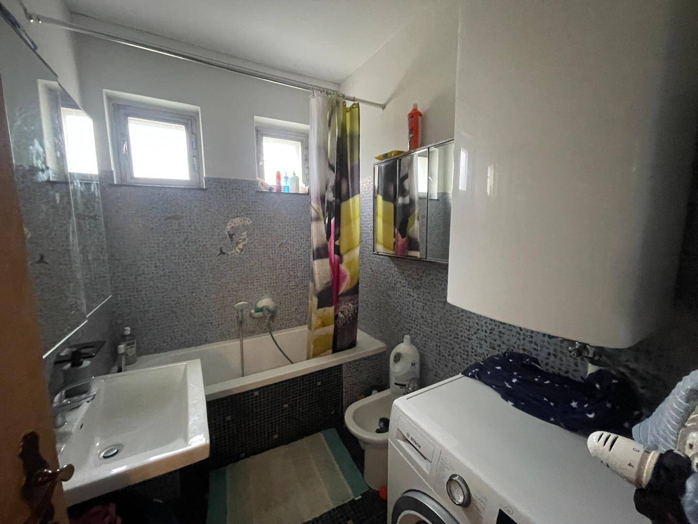 Funktionales Badezimmer mit Badewanne, Waschbecken, Bidet und Waschmaschine, ausgestattet mit kleinen Fliesen.