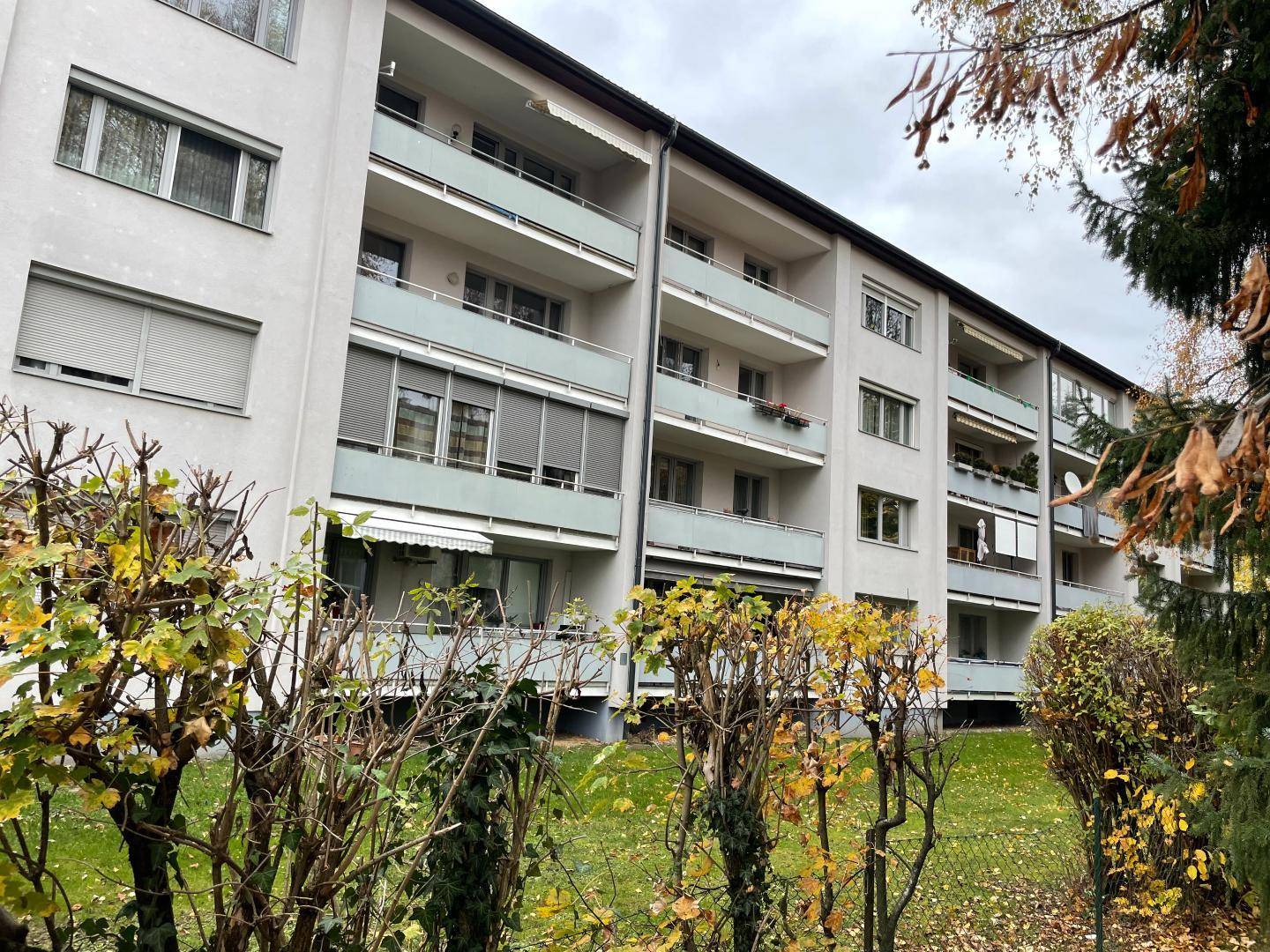 Mehrfamilienhaus mit mehreren Balkonen und Grünflächen im Vordergrund.