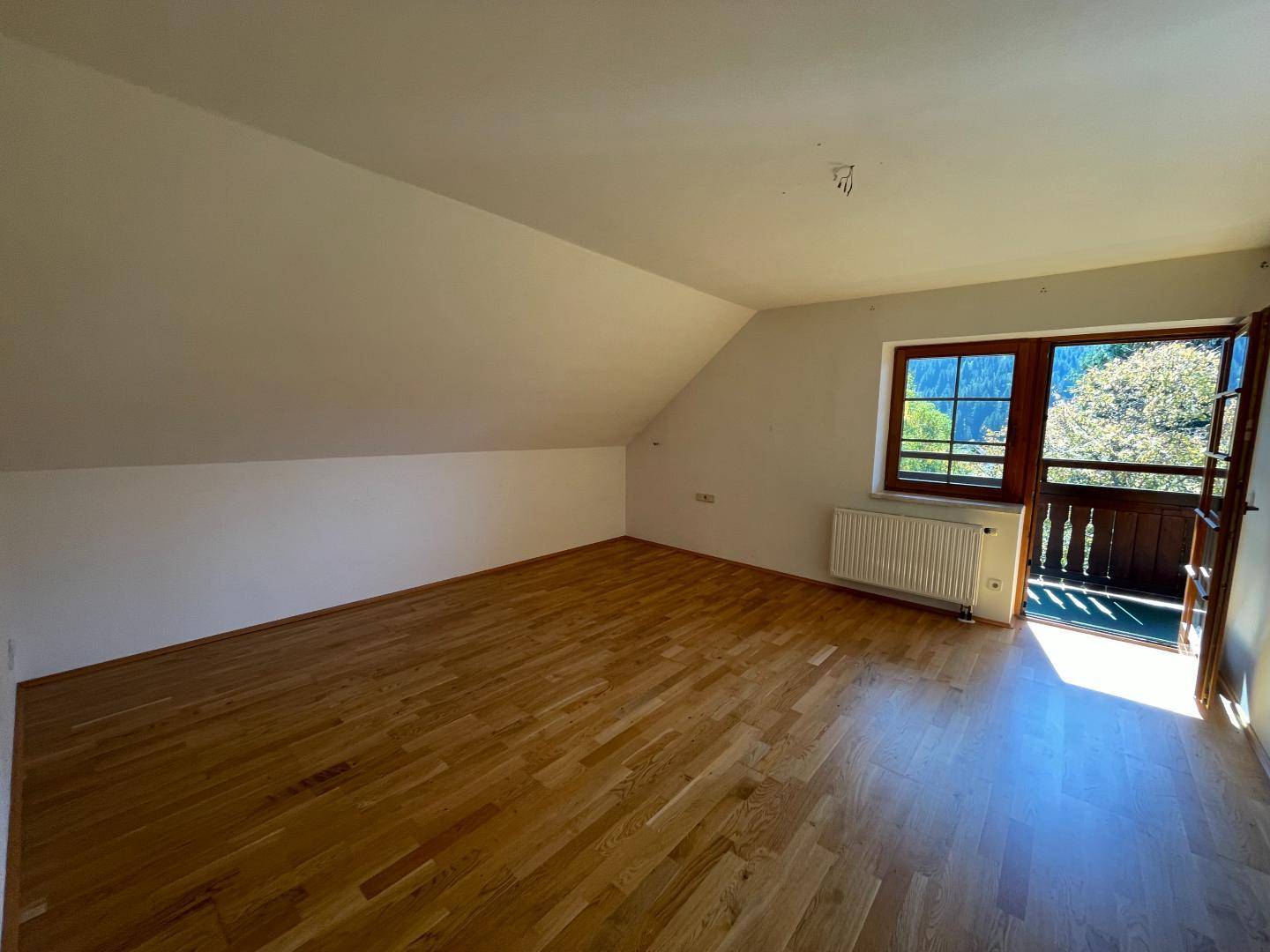 Geräumiger Raum im Dachgeschoss mit Holzboden, Dachschräge und Zugang zu einem Balkon mit Bergblick.