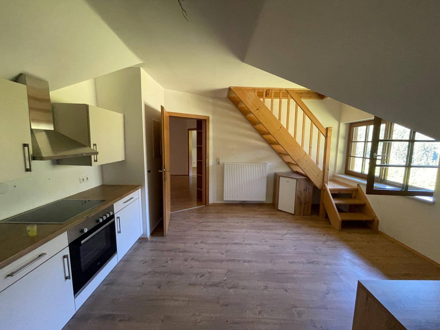 Helle Wohnküche im Dachgeschoss mit Einbauküche, Laminatboden und Holztreppe zum oberen Bereich.