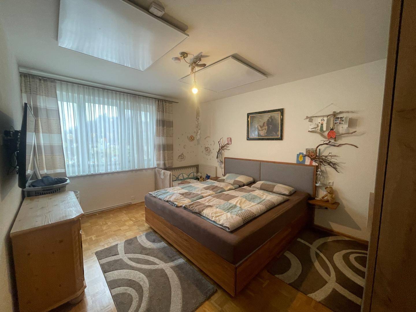 Schlafzimmer mit Doppelbett, Holzparkett und großem Fenster für viel Tageslicht.