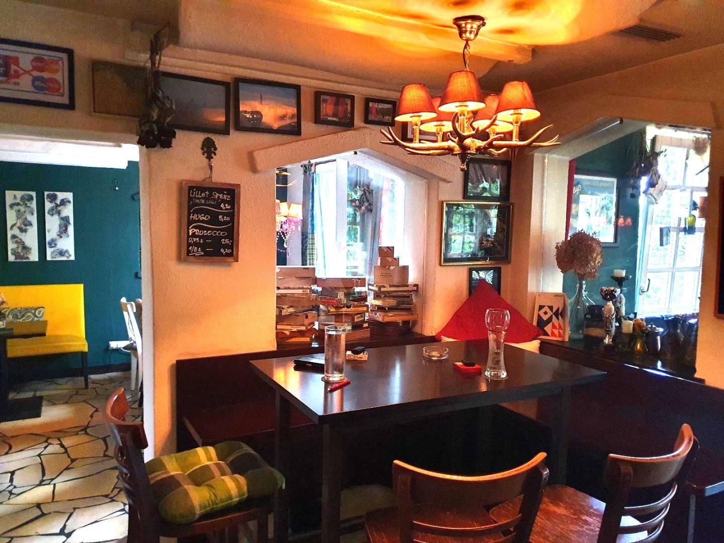 Rustikaler Essbereich mit dunklem Holztisch, Sitzbänken und einem Kronleuchter, umgeben von Bildern und einer Tafel.