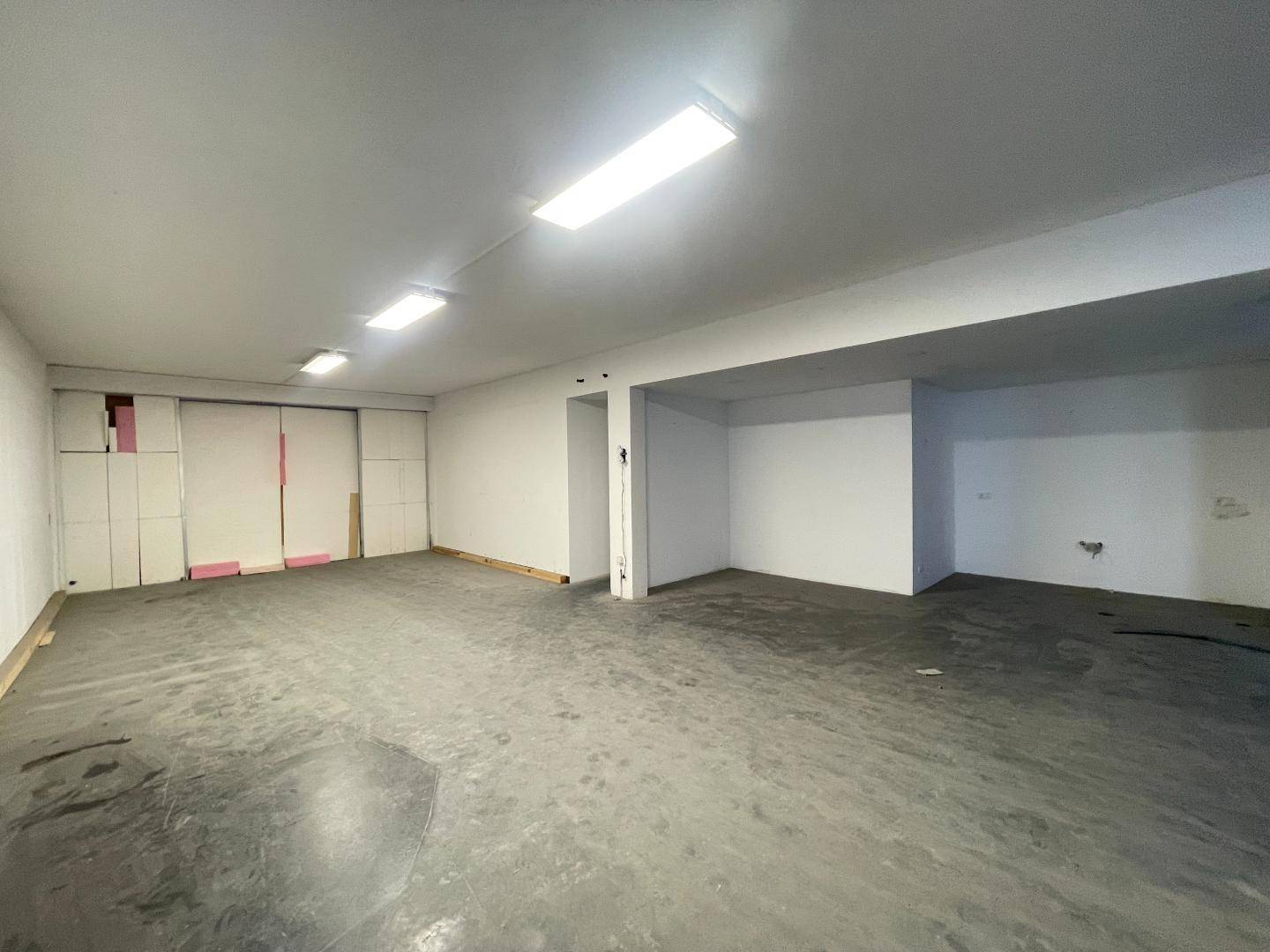 Leerer Raum mit Betonboden und Deckenbeleuchtung, geeignet als Lagerfläche oder Werkstattbereich.
