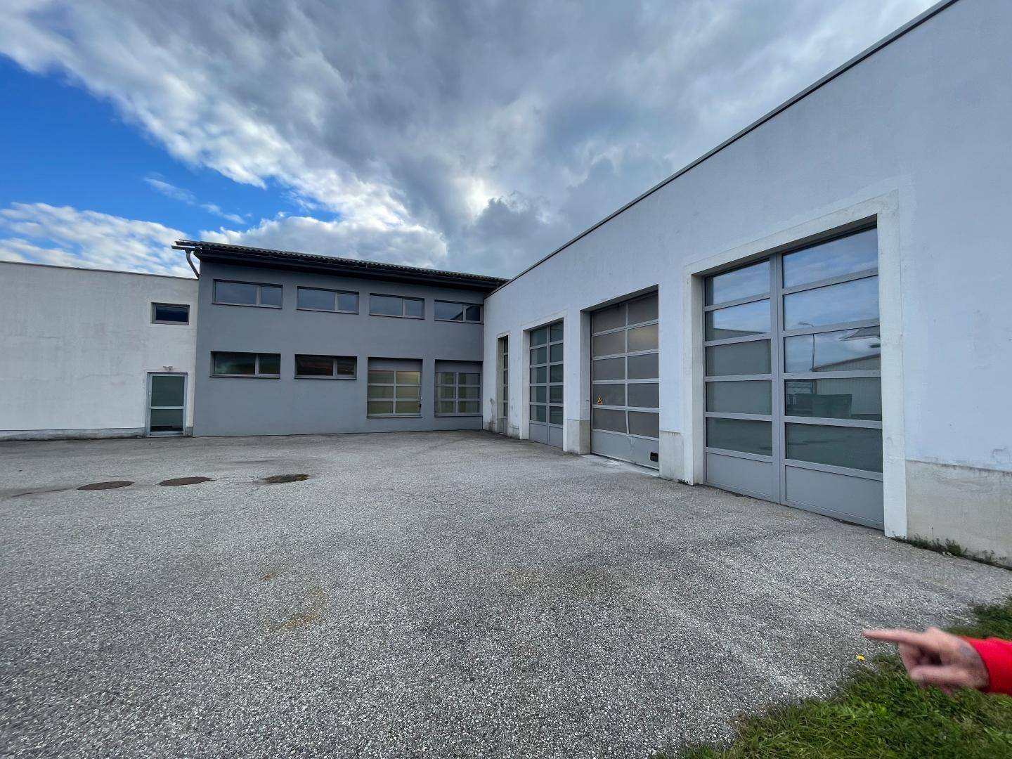 Außenansicht des Gewerbegebäudes mit Garagentoren, grauer Fassade und einem weitläufigen gepflasterten Parkplatz.