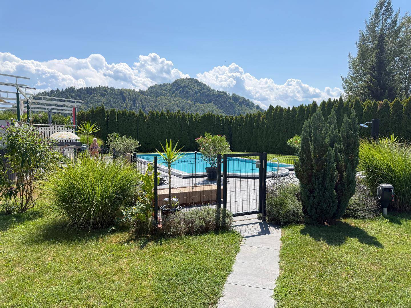 Gepflegter Gartenbereich mit Swimmingpool, hohen Hecken und malerischem Bergblick im Hintergrund.