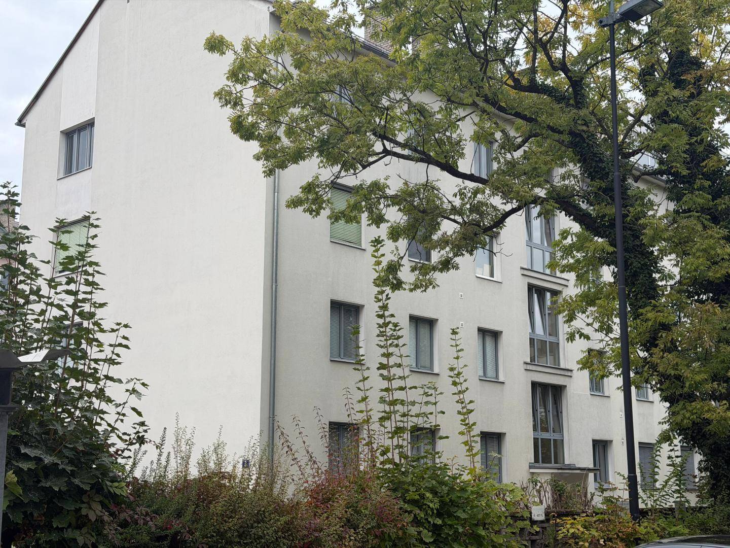 Seitenansicht eines Wohngebäudes mit mehreren Fenstern und umgebender Vegetation.