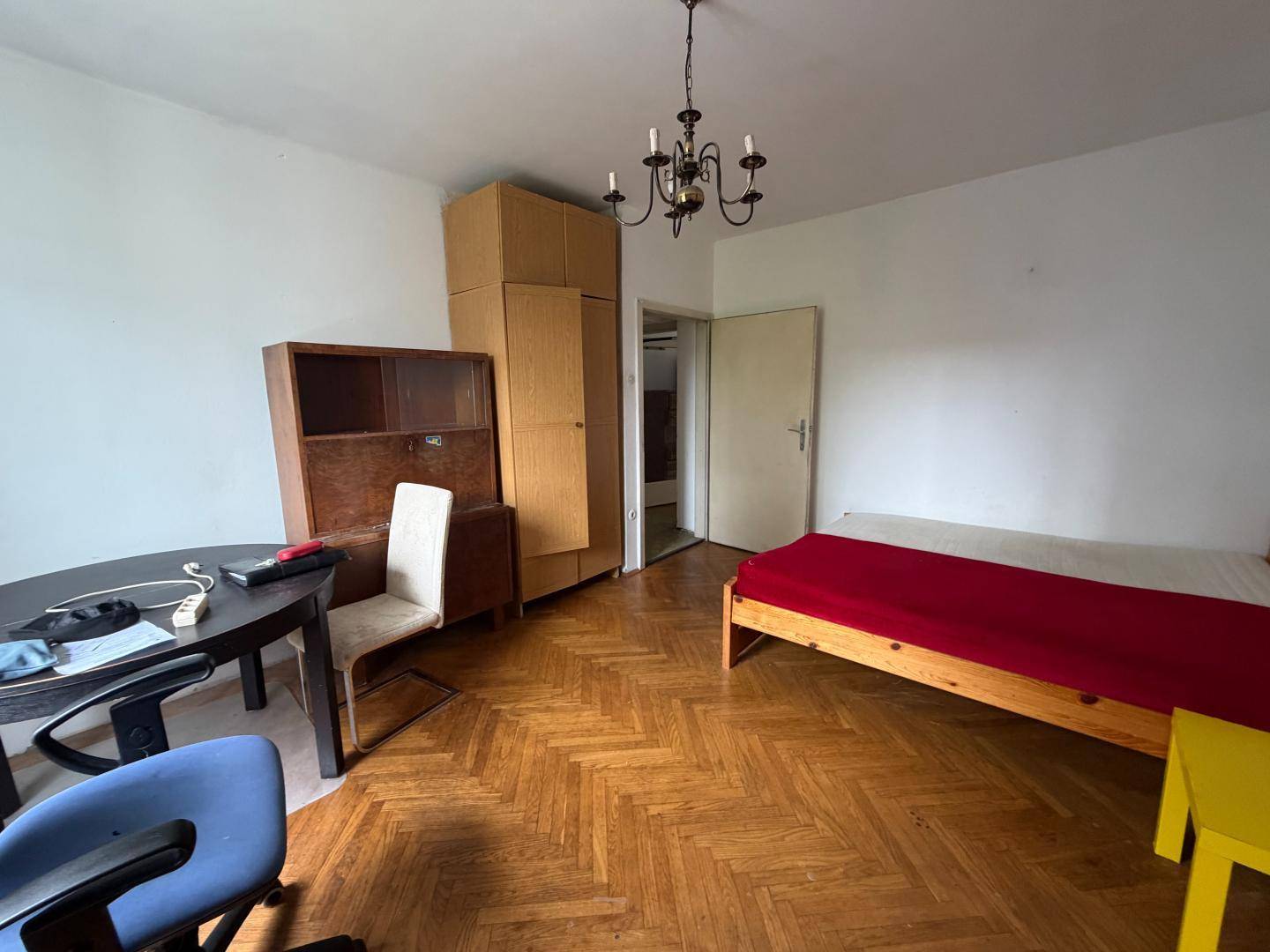 Schlafzimmer mit Fischgrätparkett, einem Bett und einem Schreibtischbereich.