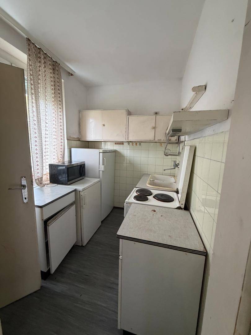 Kleine, funktionale Küche mit älteren weißen Schränken und Geräten in schlichtem Design.