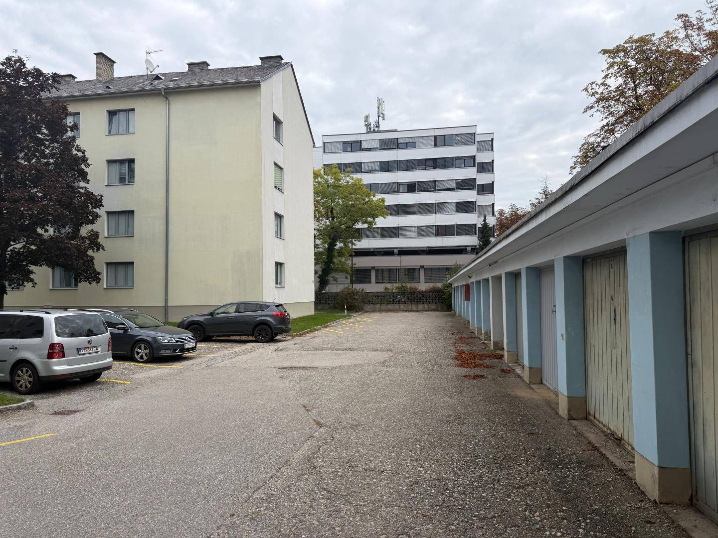 Außenbereich mit Parkplätzen, Garagenreihen und weiteren Wohngebäuden im Hintergrund.