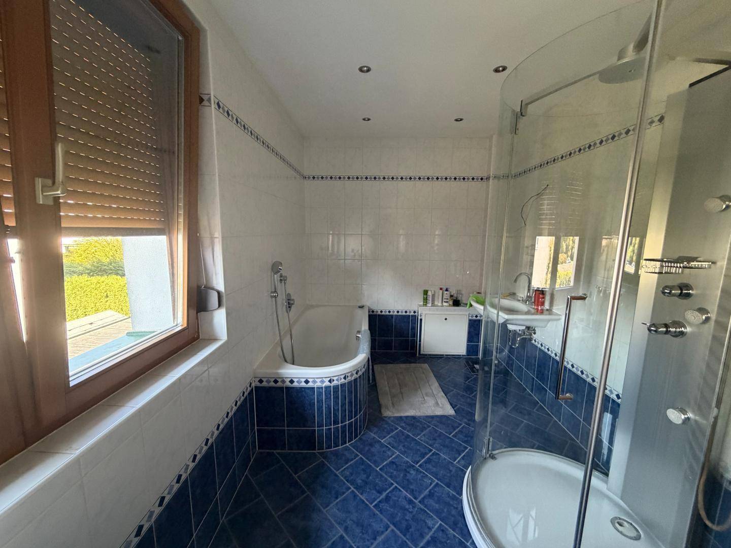 Badezimmer mit blauen und weißen Fliesen, Badewanne und moderner Duschkabine mit Glasabtrennung.