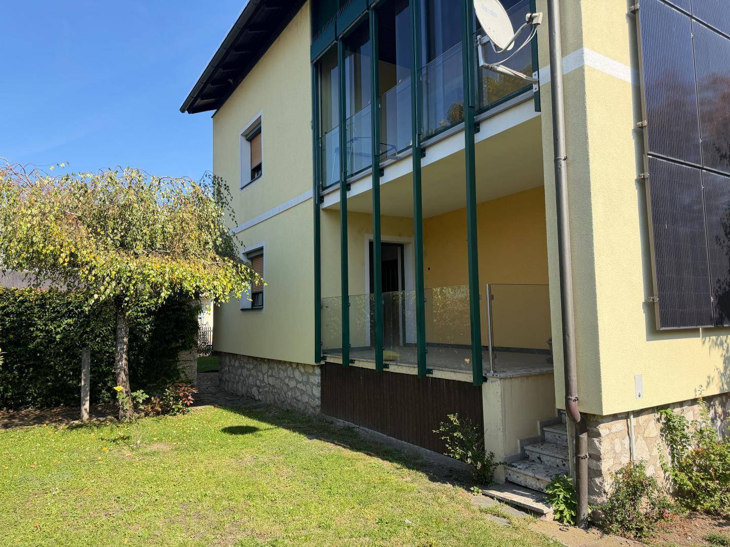 Grüner Gartenbereich neben dem Haus mit Baumbestand und Zugang zur Terrasse.