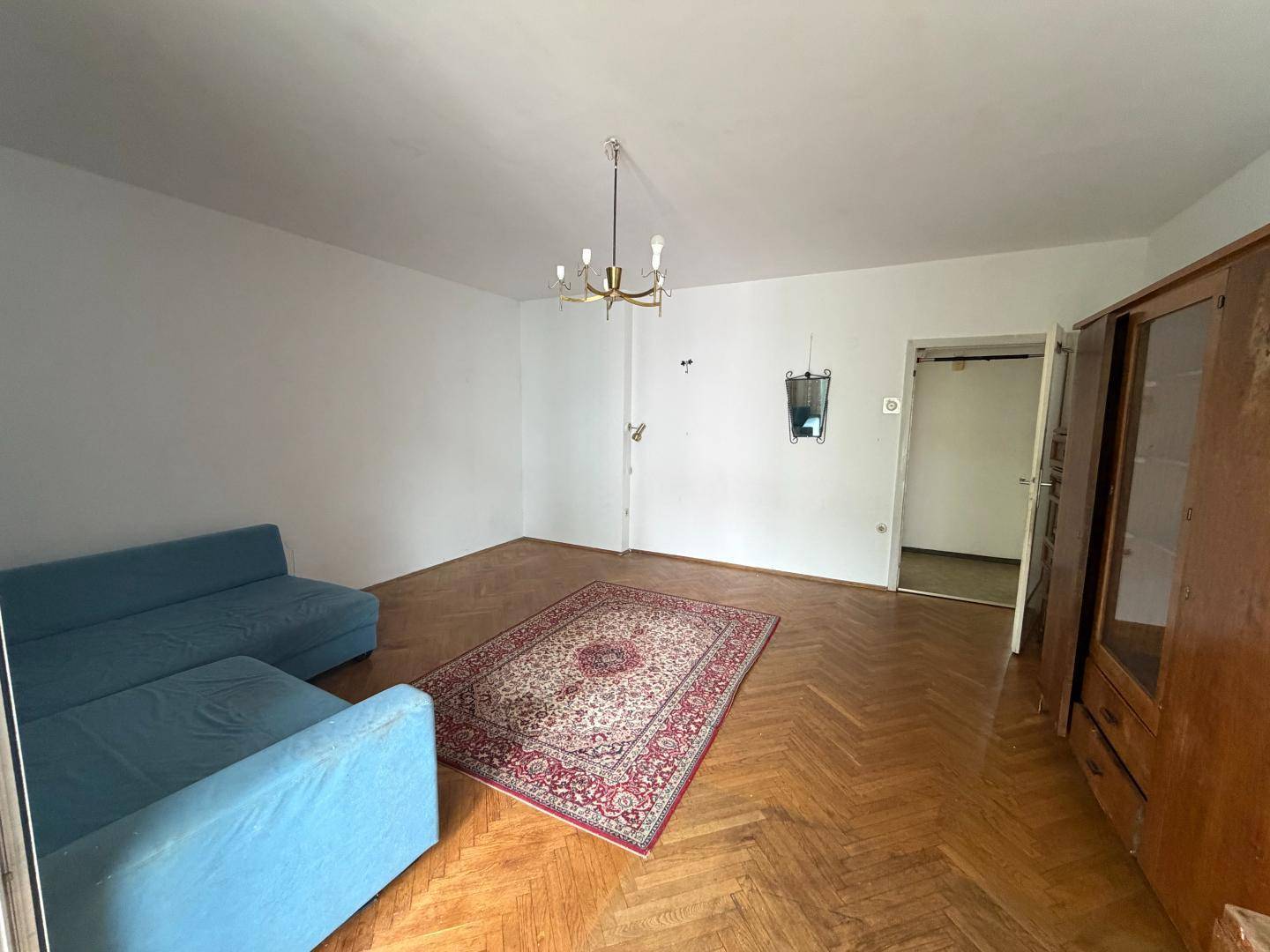 Wohnzimmer mit Fischgrätparkett, einem blauen Sofa, einem traditionellen Teppich und hohen Decken.