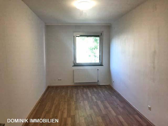 Leeres Zimmer mit Laminatboden und einem Fenster, das viel Tageslicht hereinlässt.