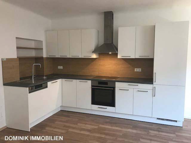 Moderne Einbauküche mit weißen Fronten und dunkler Arbeitsplatte in einem offenen Wohnbereich.