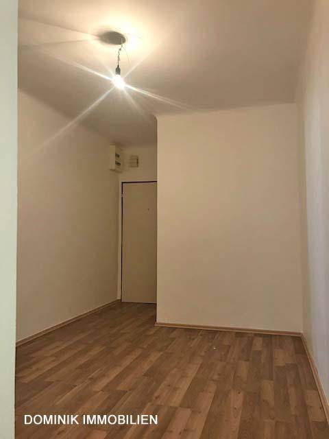Helles, unmöbliertes Zimmer mit Laminatboden und einer Tür im Hintergrund, vielseitig nutzbar.