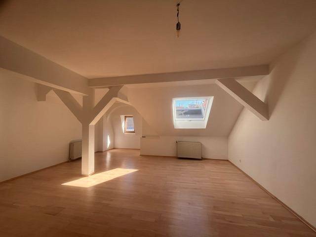 Geräumiger Wohnbereich im Dachgeschoss mit Holzboden, Dachfenster und sichtbaren Balken.